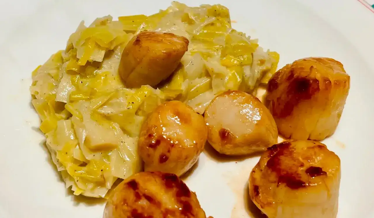 Saint-Jacques poêlées sur un lit de fondue de poireaux crémeuse, un plat savoureux et réconfortant.