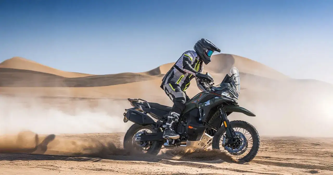 Motociclista su una CFmoto KTM sfreccia nel deserto, sollevando polvere tra le dune.