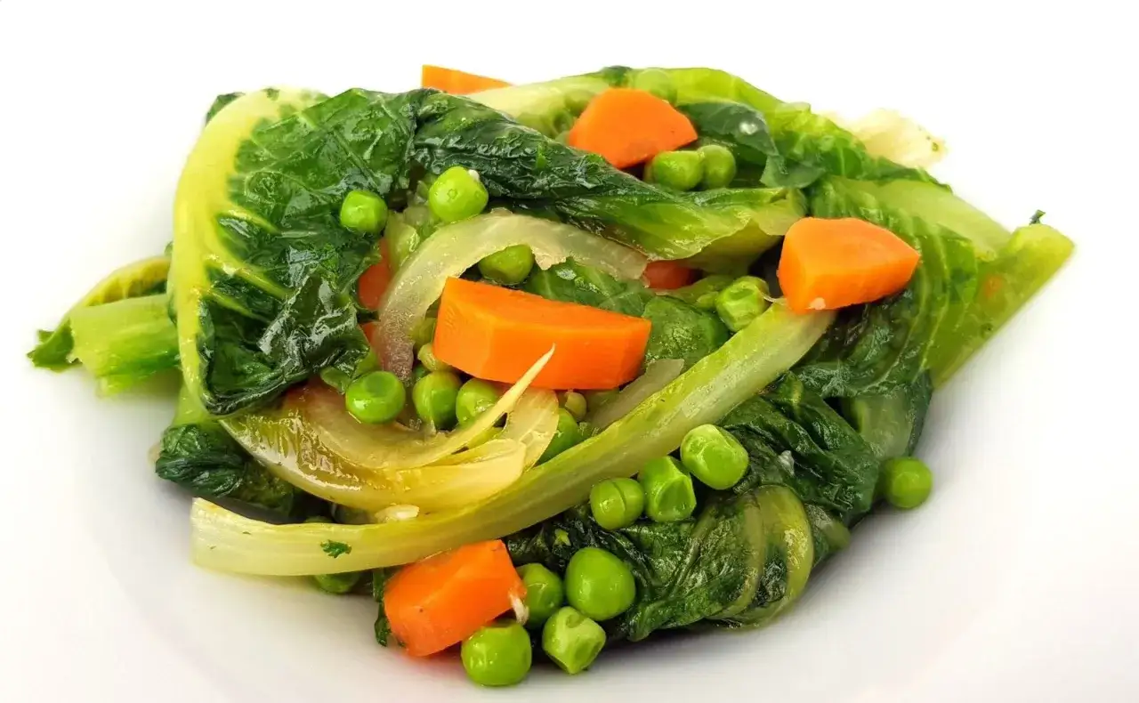 Un plat coloré de jardinière de légumes, avec des carottes, des petits pois et des feuilles vertes tendres.