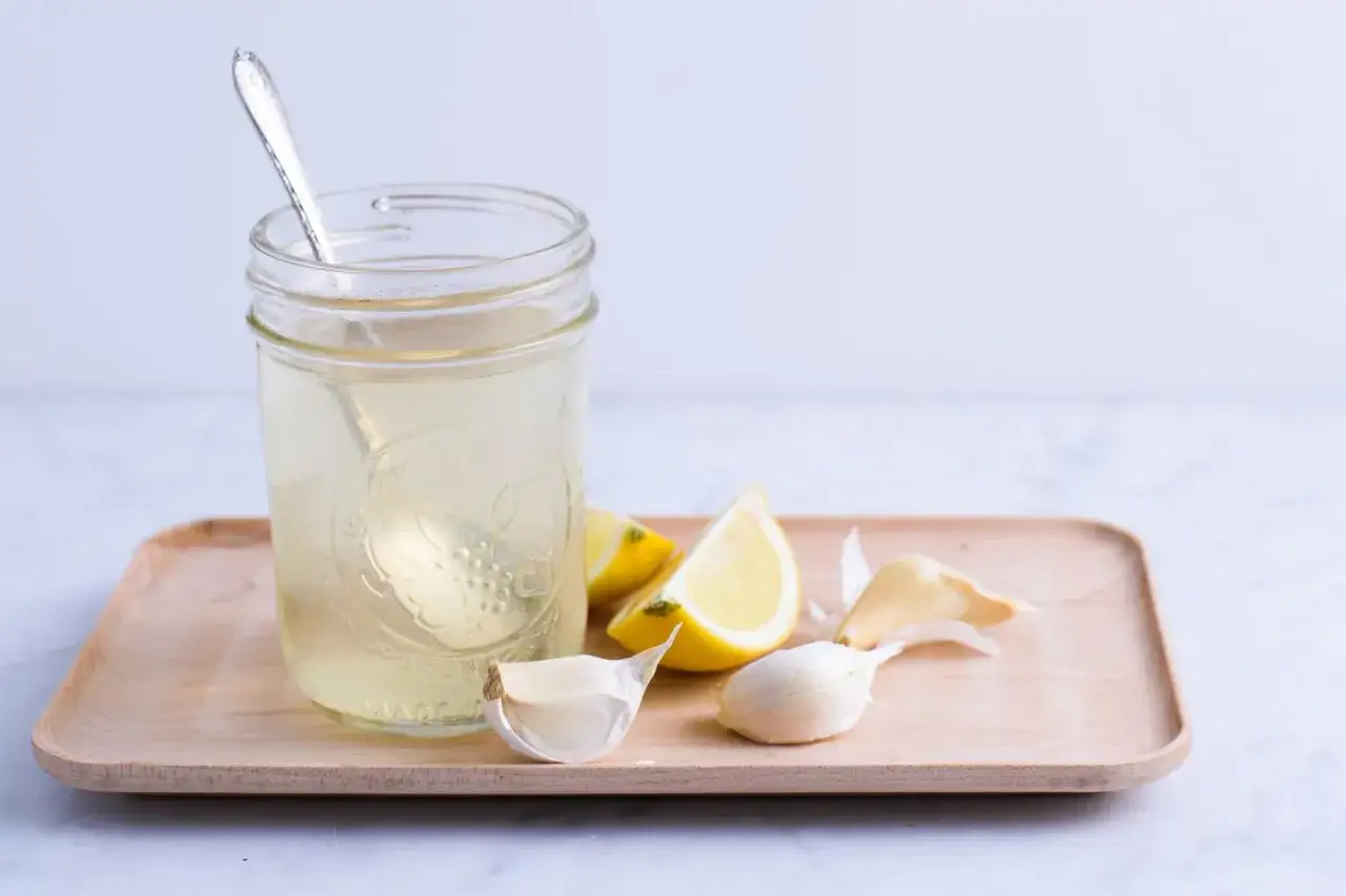 Glas mit Flüssigkeit, Zitronenspalten und Knoblauchzehen. Ein einfaches Rezept für eine Knoblauch-Zitrone-Kur.