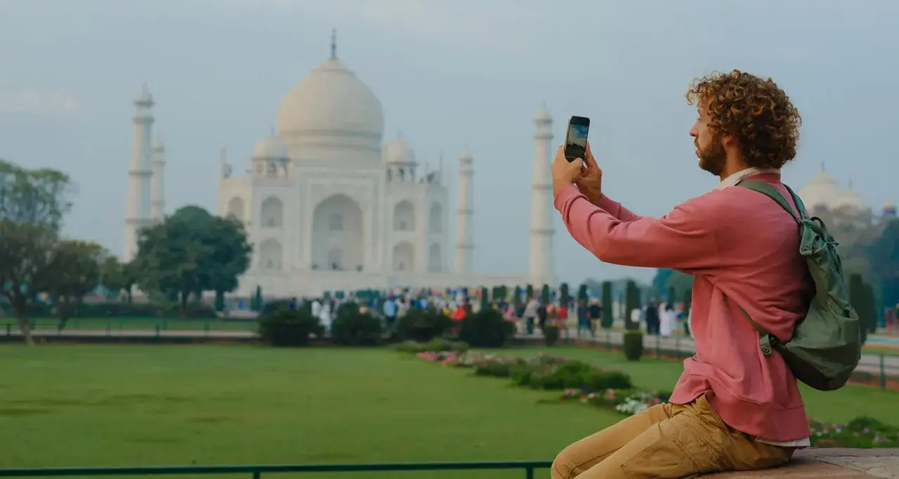 Mężczyzna z kręconymi włosami robi zdjęcie Taj Mahal w Indiach.