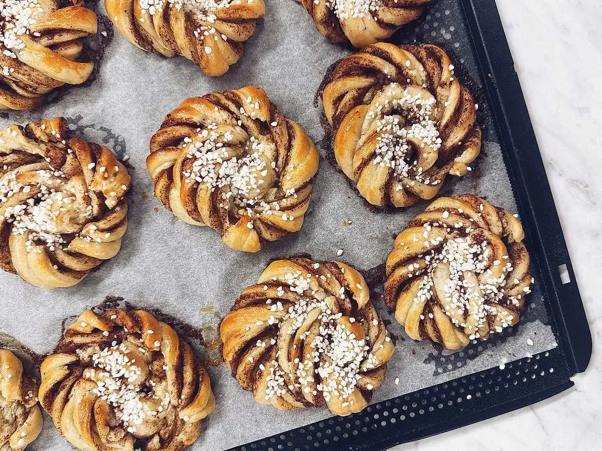 Nybakade kanelbullar med p&auml;rlsocker, redo att avnjutas. En h&auml;rlig kanelbulle l&auml;ngd p&aring; bakpl&aring;tspapper.