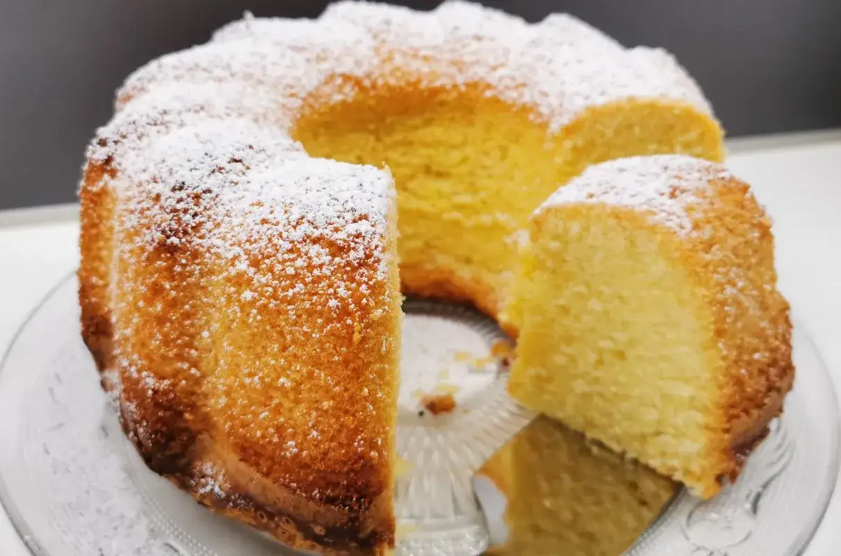 Wilgotna babka z ajerkoniakiem, oprószona cukrem pudrem, prezentuje się apetycznie na szklanej paterze.