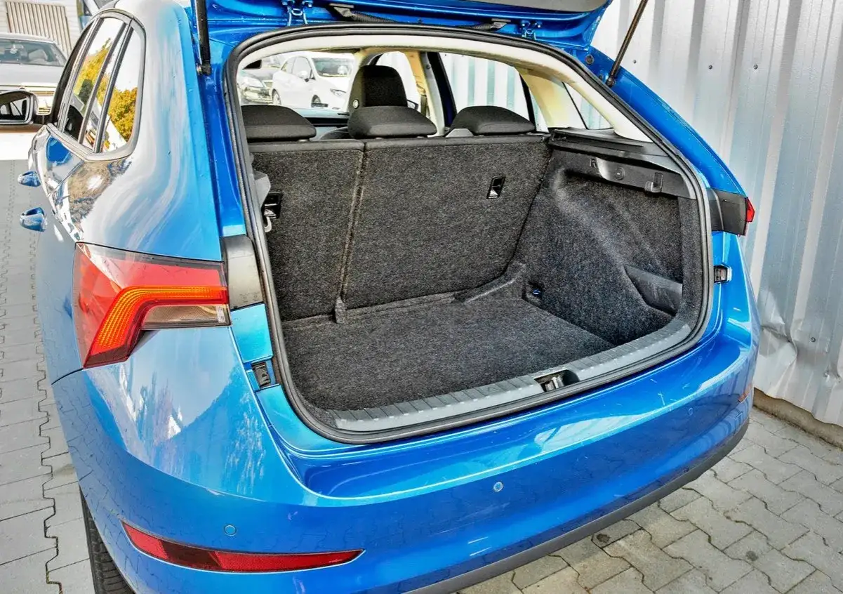 Błękitna Skoda Scala z otwartym bagażnikiem. Wnętrze jest wyłożone wykładziną, a siedzenia złożone. Wymiary bagażnika są imponujące.