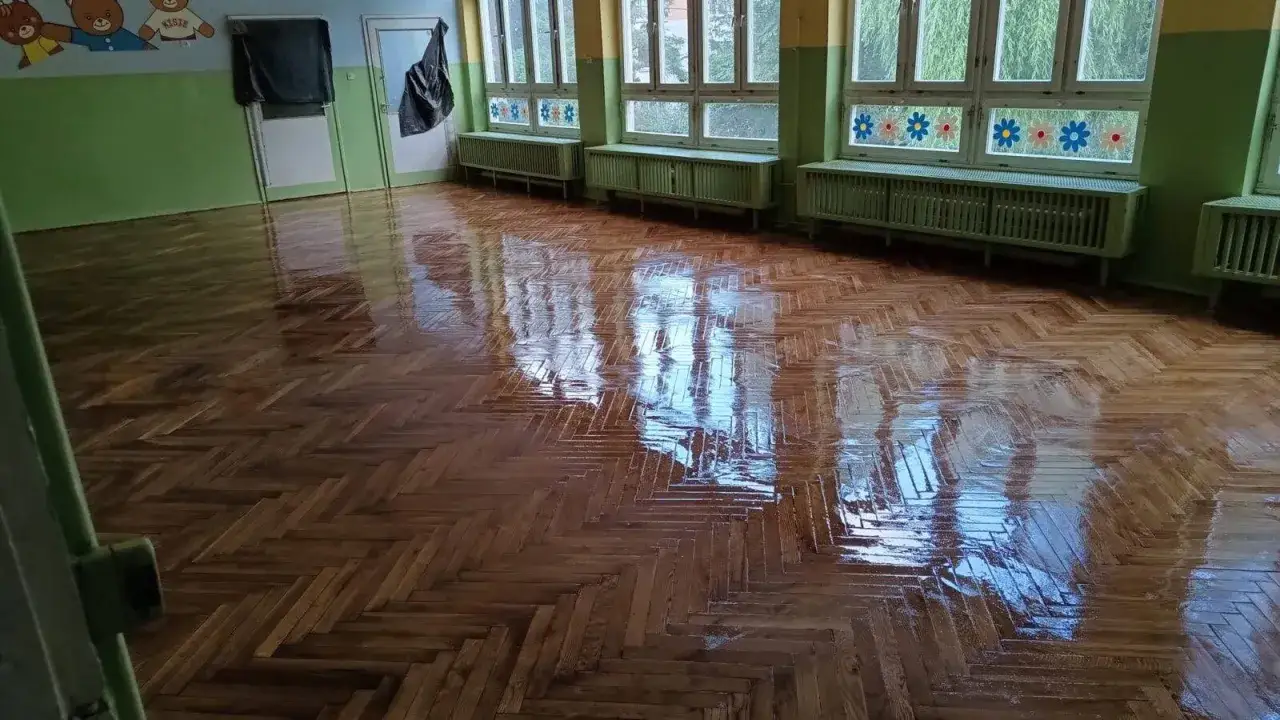 Błyszcząca, świeżo odnowiona podłoga z parkietu w pomieszczeniu z oknami i kaloryferami.
