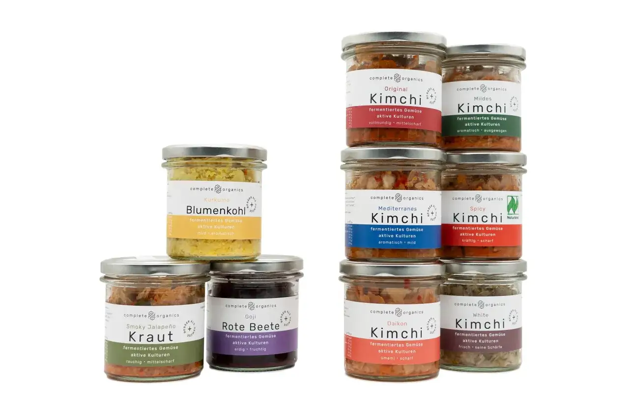 Verschiedene Gl&auml;ser mit fermentiertem Gem&uuml;se, darunter Kimchi in diversen Sorten wie Original, Mildes, Mediterranes, Spicy, Daikon und White. Auch Blumenkohl und Rote Bete sind als 