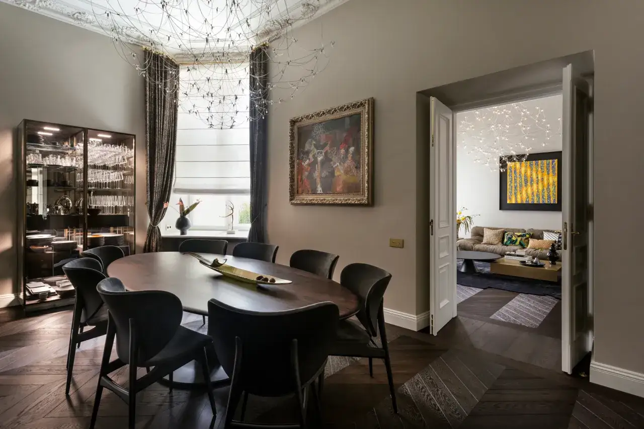 Elegancka jadalnia z owalnym stołem i krzesłami, obok przeszklona witryna. W tle salon, tworząc atmosferę jak w stylowej brasserie.