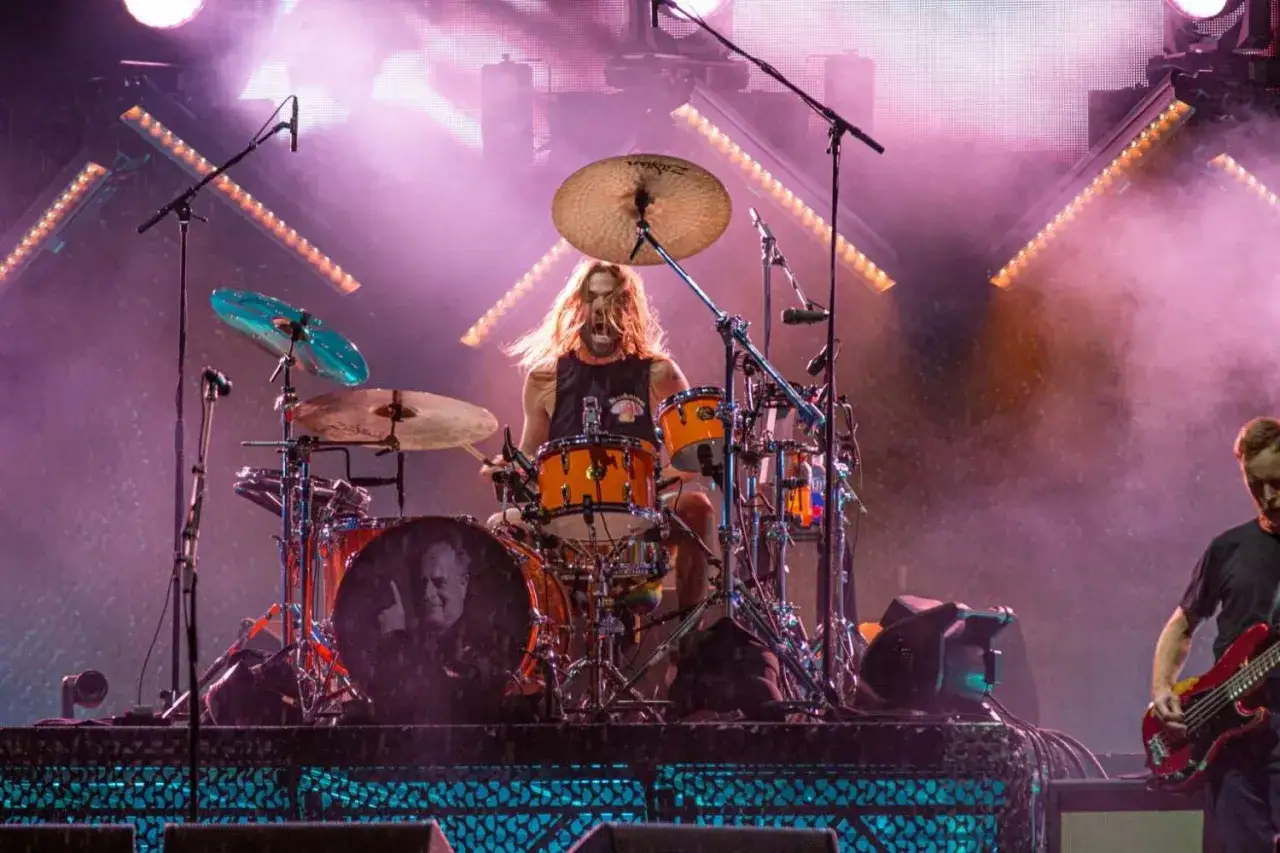 Foo Fighters perkusista, Taylor Hawkins, w swoim żywiole, z włosami rozwianymi przez wiatr i dzikim okrzykiem na ustach, uderza w pomarańczowe bębny.