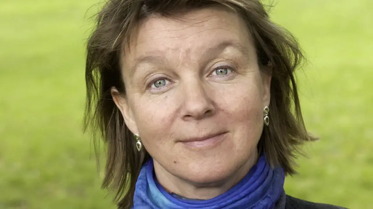 Elisabeth Rynell, med blå ögon och ett vänligt leende, bär en blå scarf och örhängen.