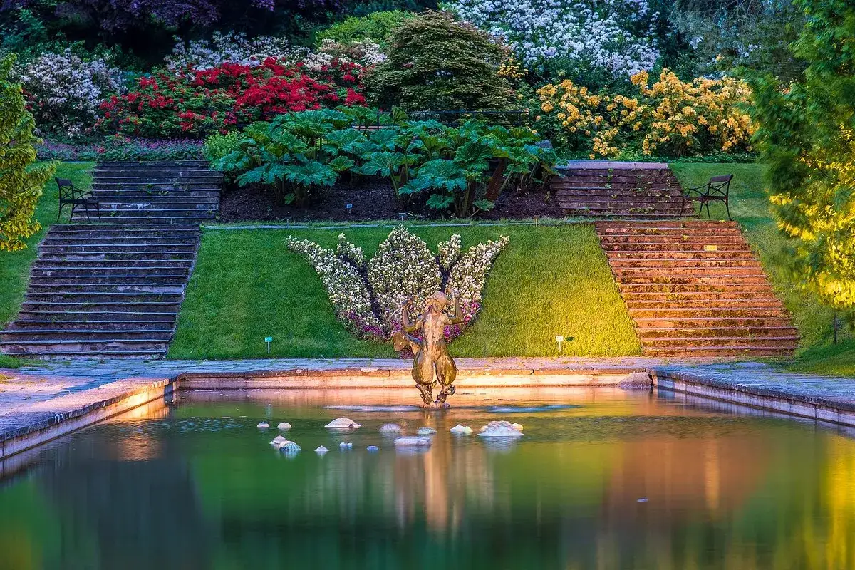 En fontän med en staty av en musiker omgiven av blommor i en vacker damm. Trappor leder upp till en frodig, blomstrande sluttning i botaniska trädgården i Göteborg.