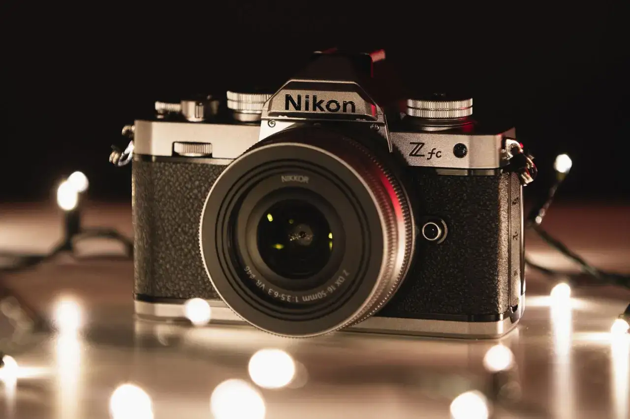 Retro aparat Nikon Z fc z obiektywem NIKKOR, otoczony świątecznymi lampkami. Zastanawiasz się, ile kosztuje aparat tej klasy?