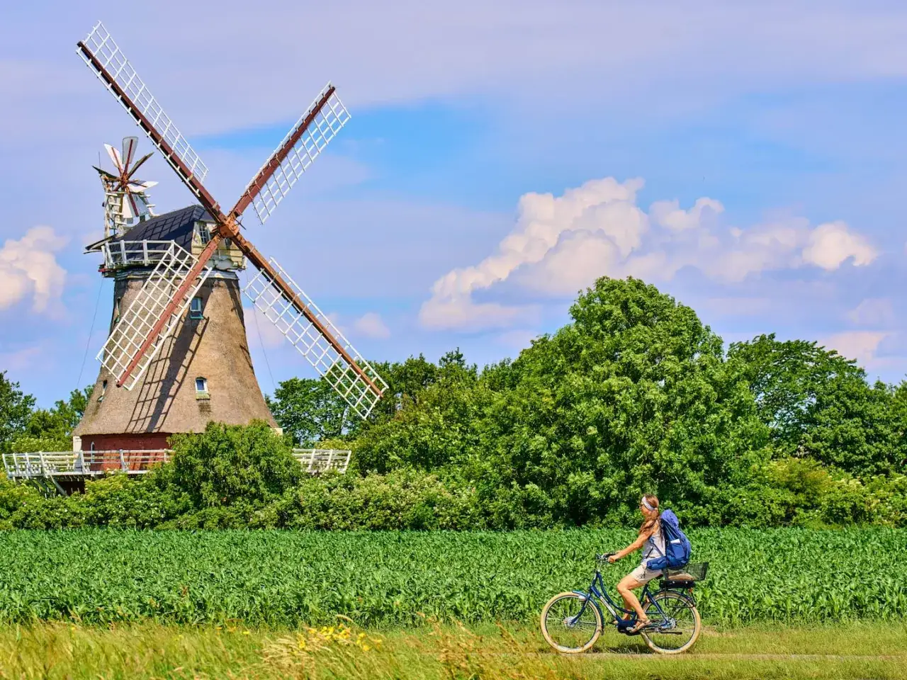 Frau radelt an einem historischen Windrad vorbei, ein Geheimtipp f&uuml;r Radwege.