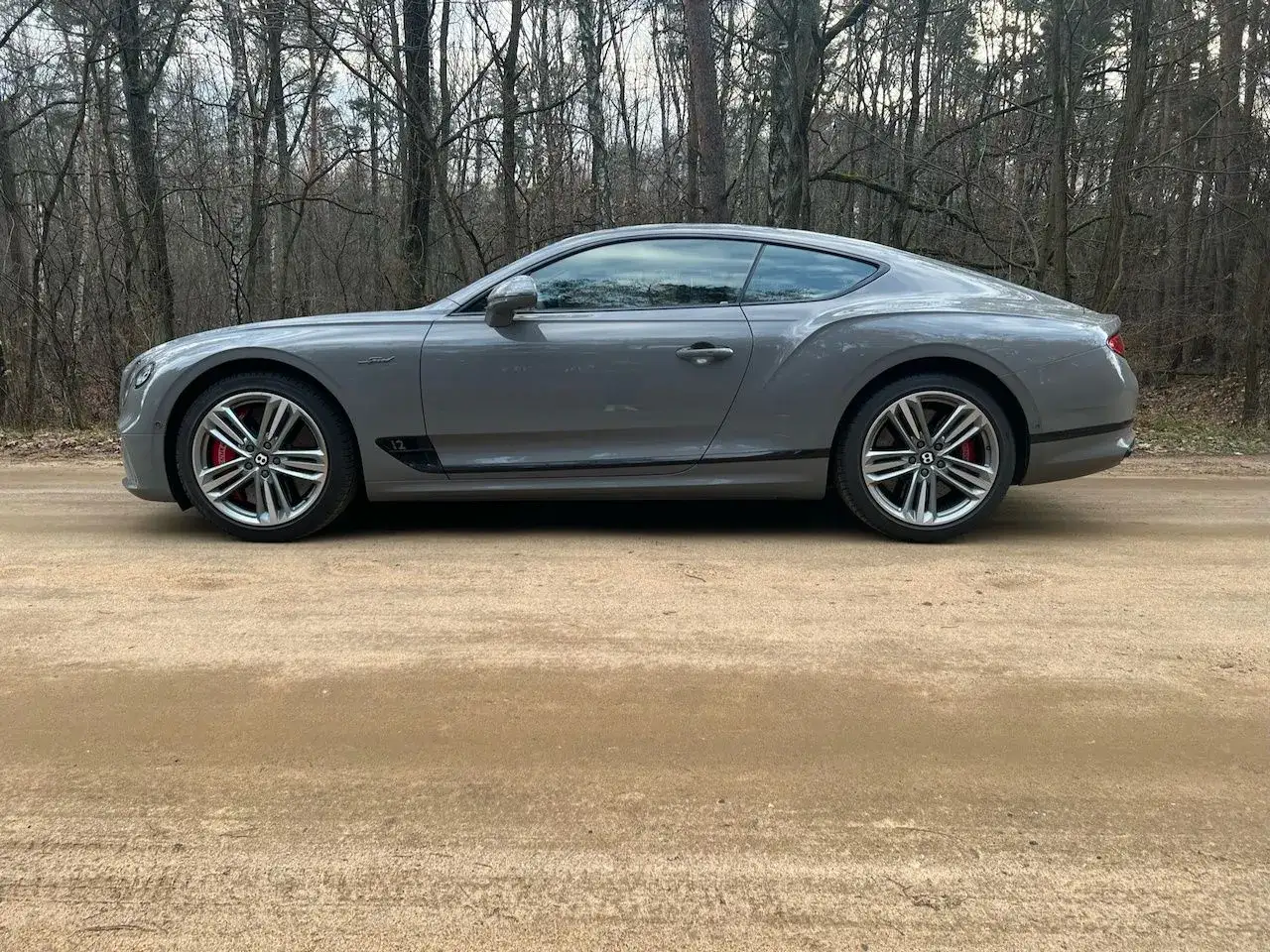 Szary Bentley Continental GT na leśnej drodze. Zastanawiasz się nad bentley continental gt cena?