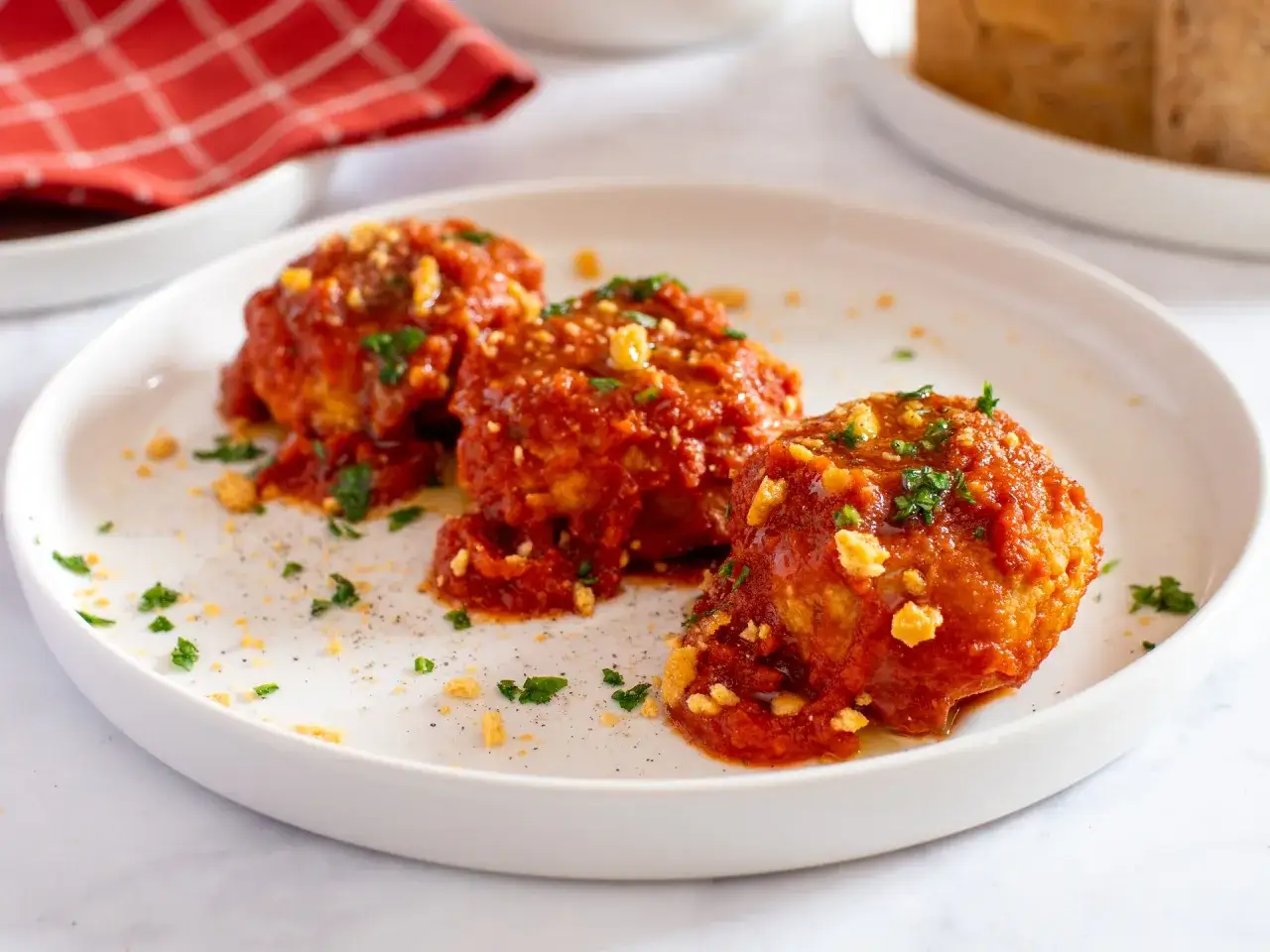 Tre polpette di pane al sugo, ricoperte di salsa rossa e prezzemolo tritato, su un piatto bianco.
