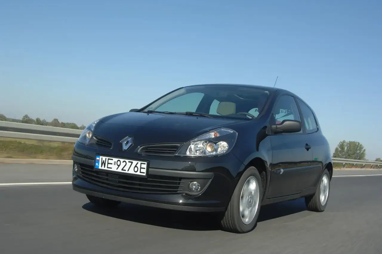 Czarny Renault Clio 3 1.2 benzyna pędzi po drodze, błyszcząc w słońcu.