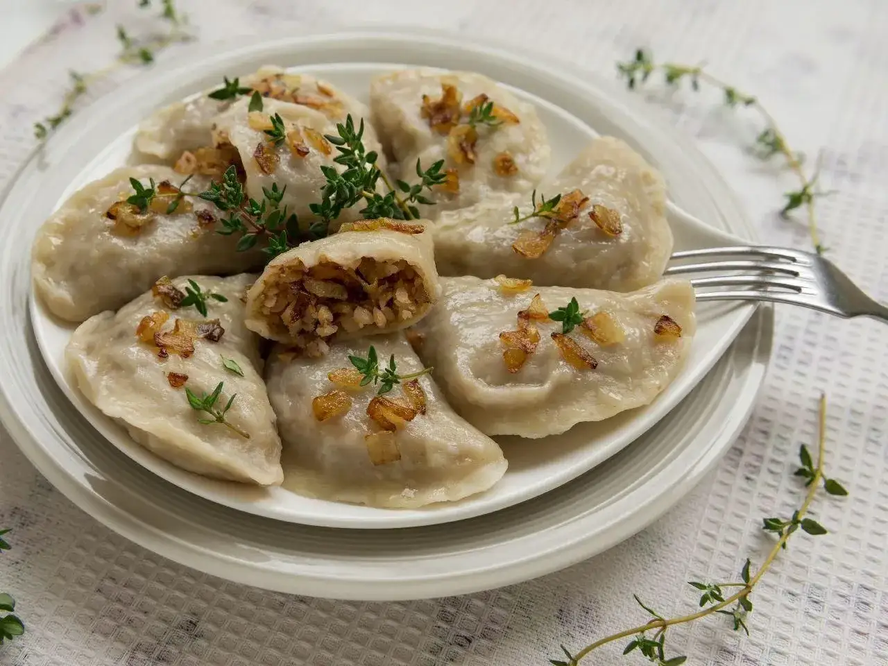 Pyszne pierogi z kaszą gryczaną, okraszone chrupiącą cebulką i świeżym tymiankiem, czekają na talerzu.