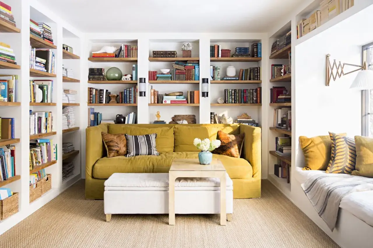 Sala acogedora con sof&aacute; amarillo, estanter&iacute;as llenas de libros, ideal para saber qu&eacute; obras no necesitan licencia.