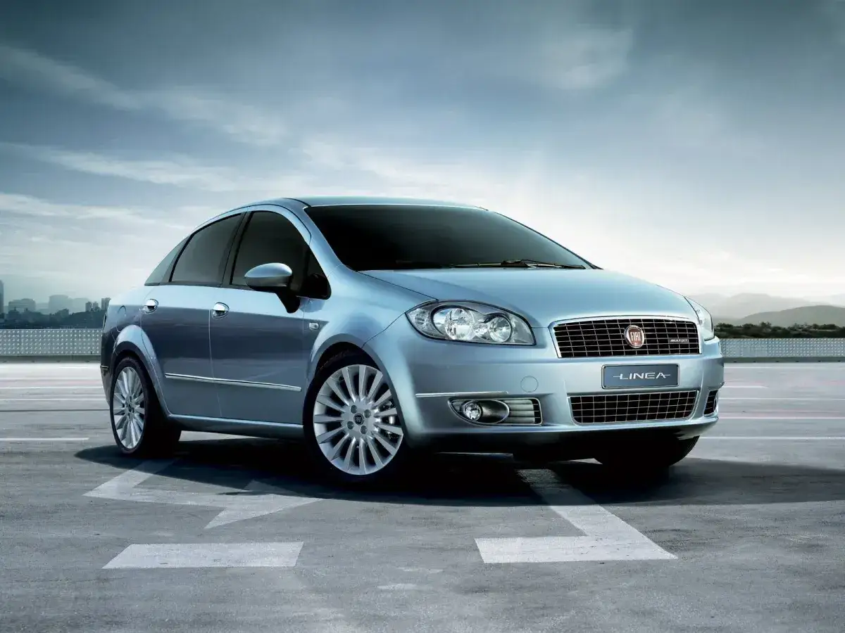 Elegancki, błękitny Fiat Linea stoi na betonowym placu z widokiem na miasto.