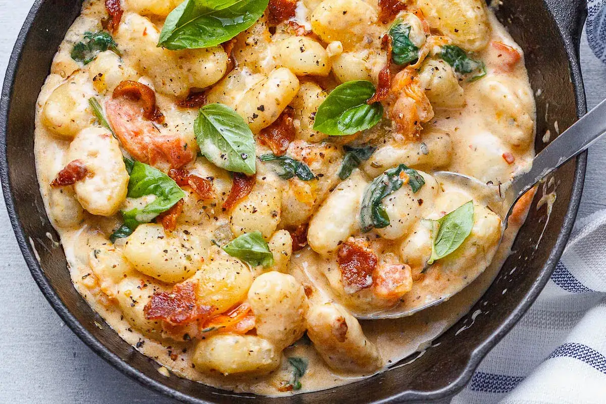 Szybkie danie z gnocchi w kremowym sosie z suszonymi pomidorami i szpinakiem, ozdobione świeżą bazylią. Idealne na szybki obiad.