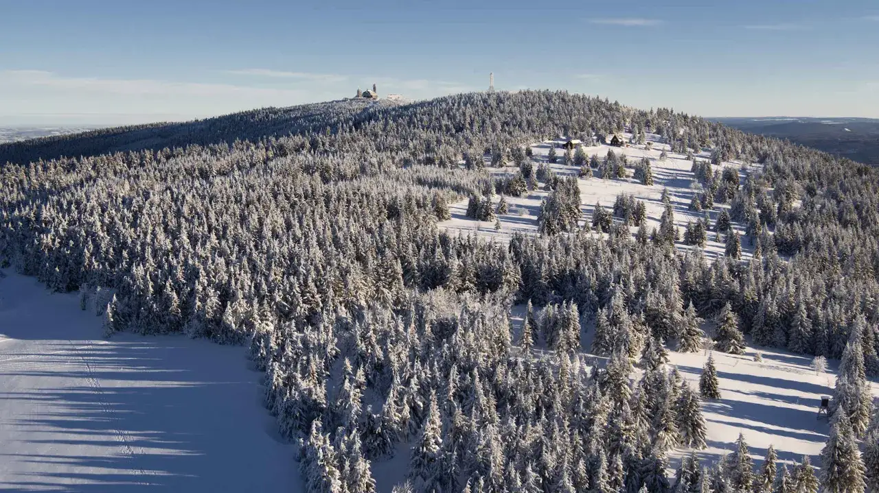 Schneebedeckter berg in Sachsen, mit Nadelb&auml;umen und Geb&auml;uden auf dem Gipfel.