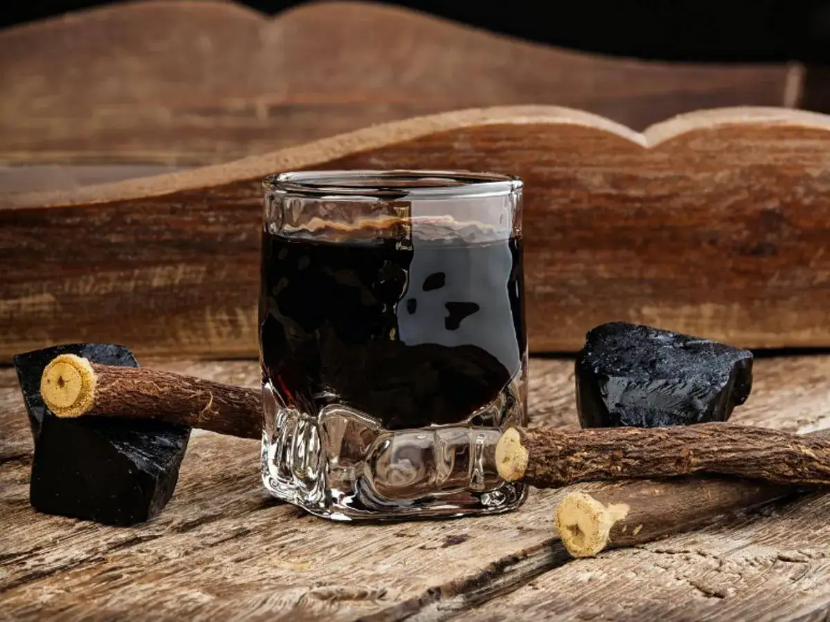 Glas mit dunklem Lik&ouml;r, daneben Lakritzst&uuml;cke und -wurzeln. Perfekt, um **Lakritz Schnaps selber machen** zu wollen.