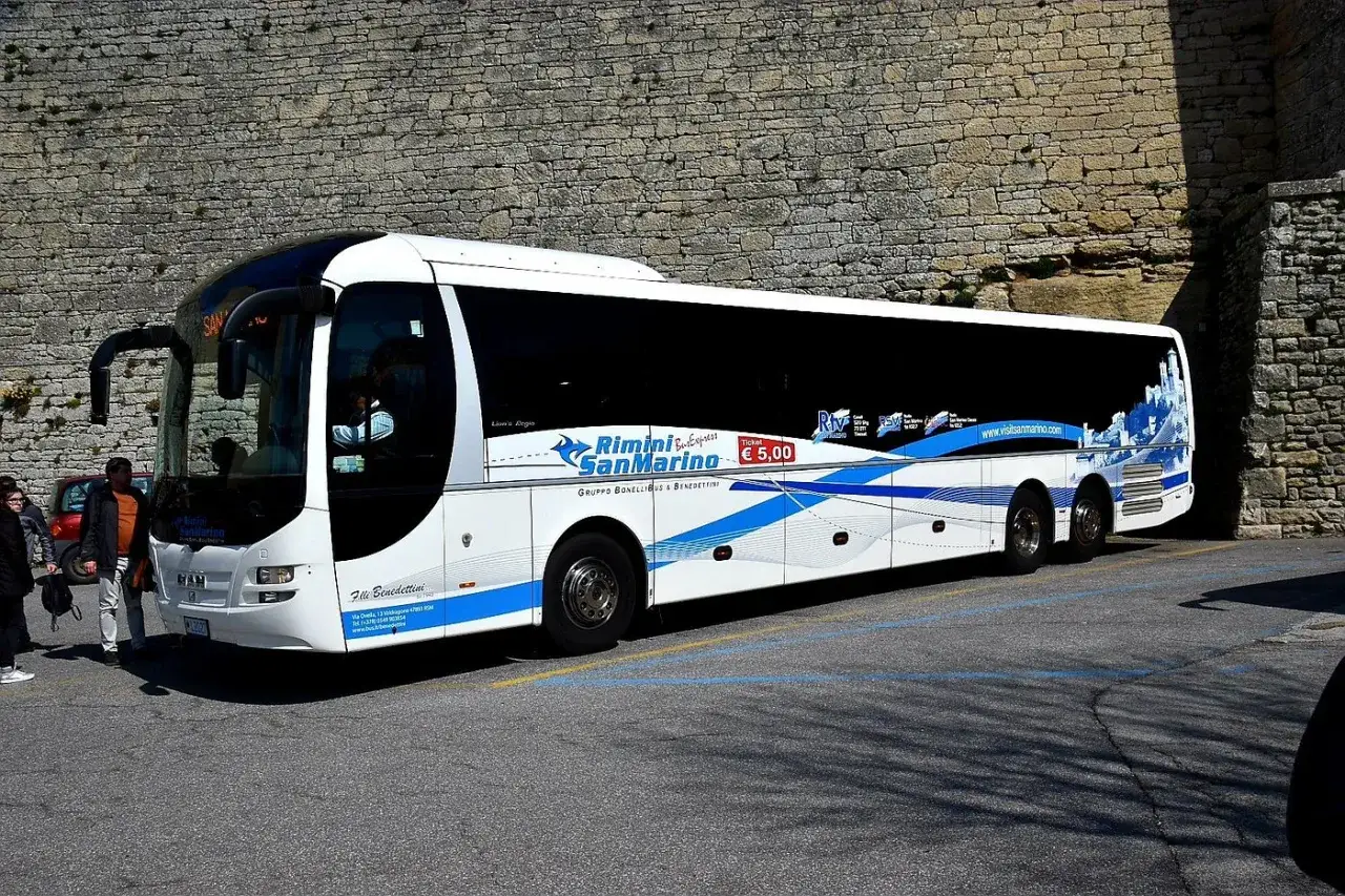 Autobus Rimini San Marino, con logo e sito web, parcheggiato vicino a un muro di pietra.
