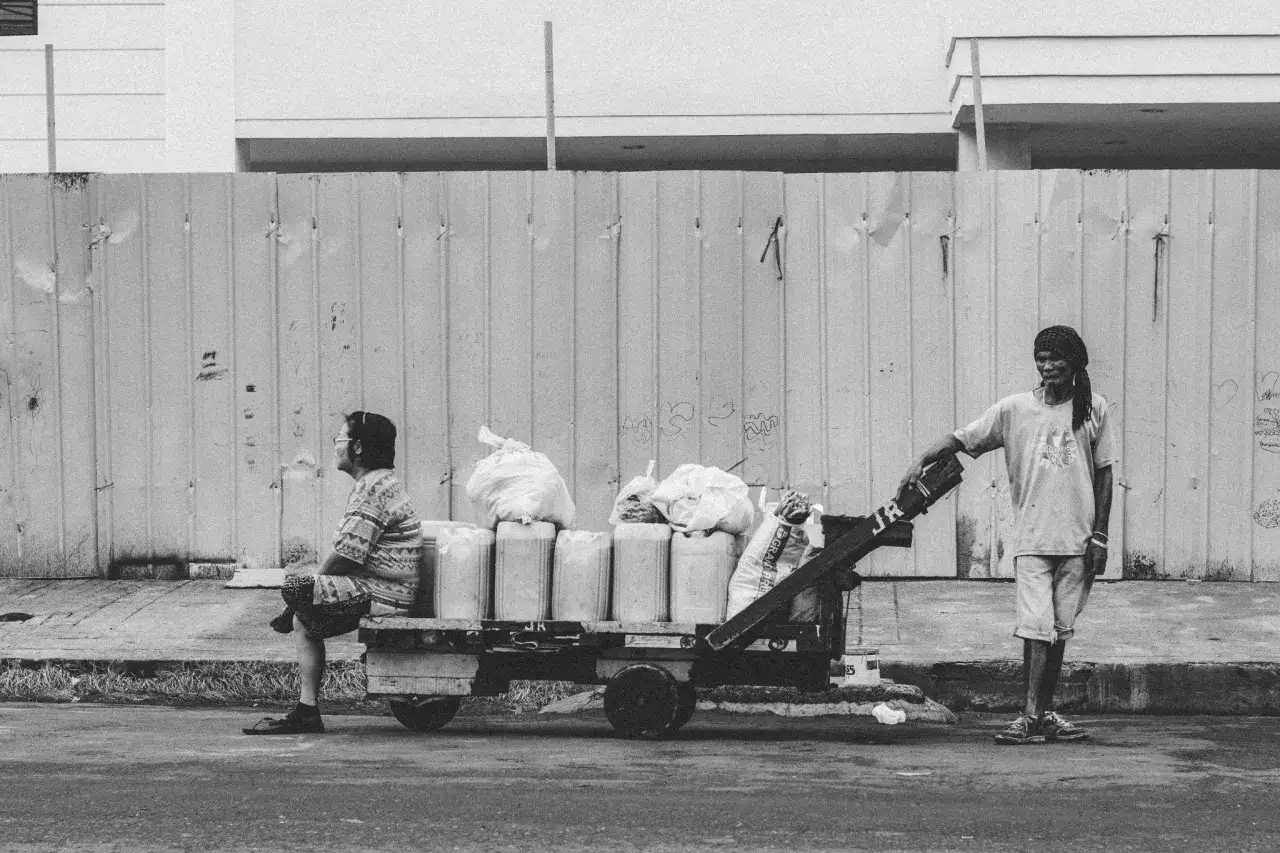 Une femme assise sur une charrette chargée de bidons et de sacs, un homme se tient à côté. Une scène de la vie quotidienne capturée dans cette série photo.