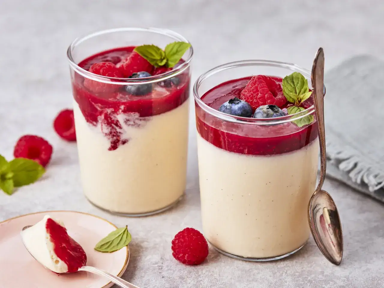 Zwei Gl&auml;ser mit cremiger bayrischer Creme, garniert mit frischen Beeren und Minze. Ein L&ouml;ffel zeigt einen Klecks des Desserts.