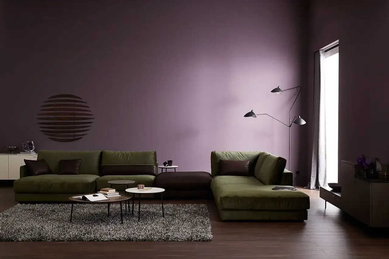Grüne Sofas und braune Akzente harmonieren perfekt mit der lila Wand. Welche Farbe passt zu Lila? Hier sehen wir eine stilvolle Antwort.