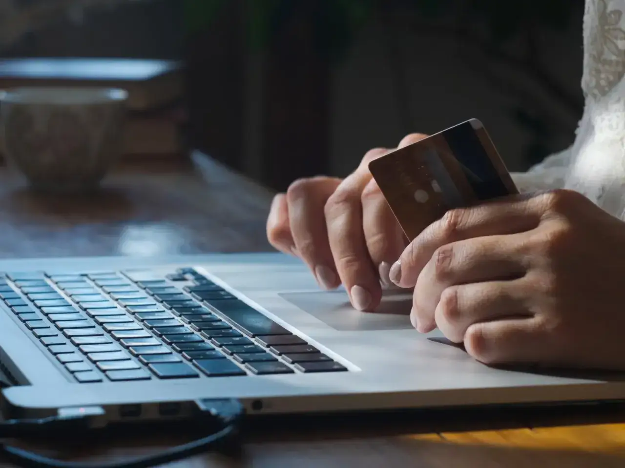 Dłonie trzymające kartę zbliżają się do laptopa, sugerując transakcję online. Zastanawiasz się, ile można wpłacić na konto?