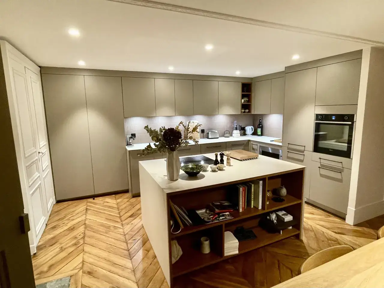 Une cuisine ouverte moderne avec un îlot central, des placards gris, un parquet en chevrons et une décoration florale.