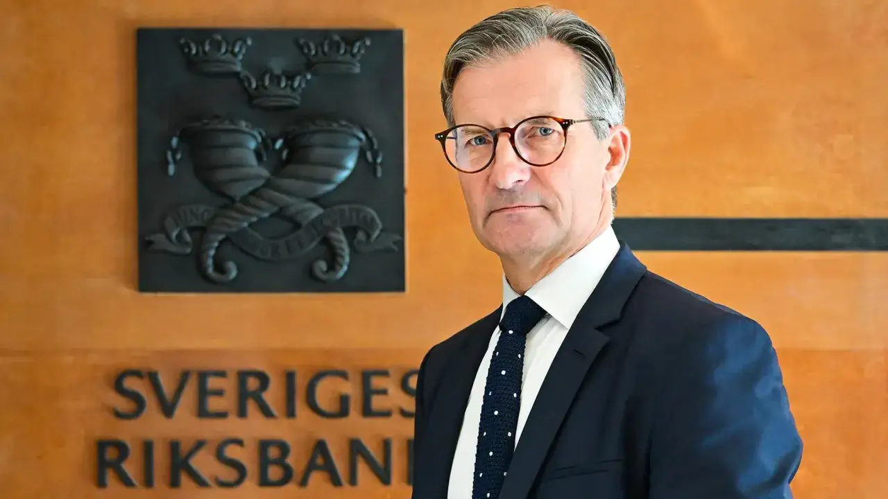 Erik Thedéen, med glasögon och kostym, står framför Sveriges Riksbank. Hans barn skulle vara stolta över hans position.