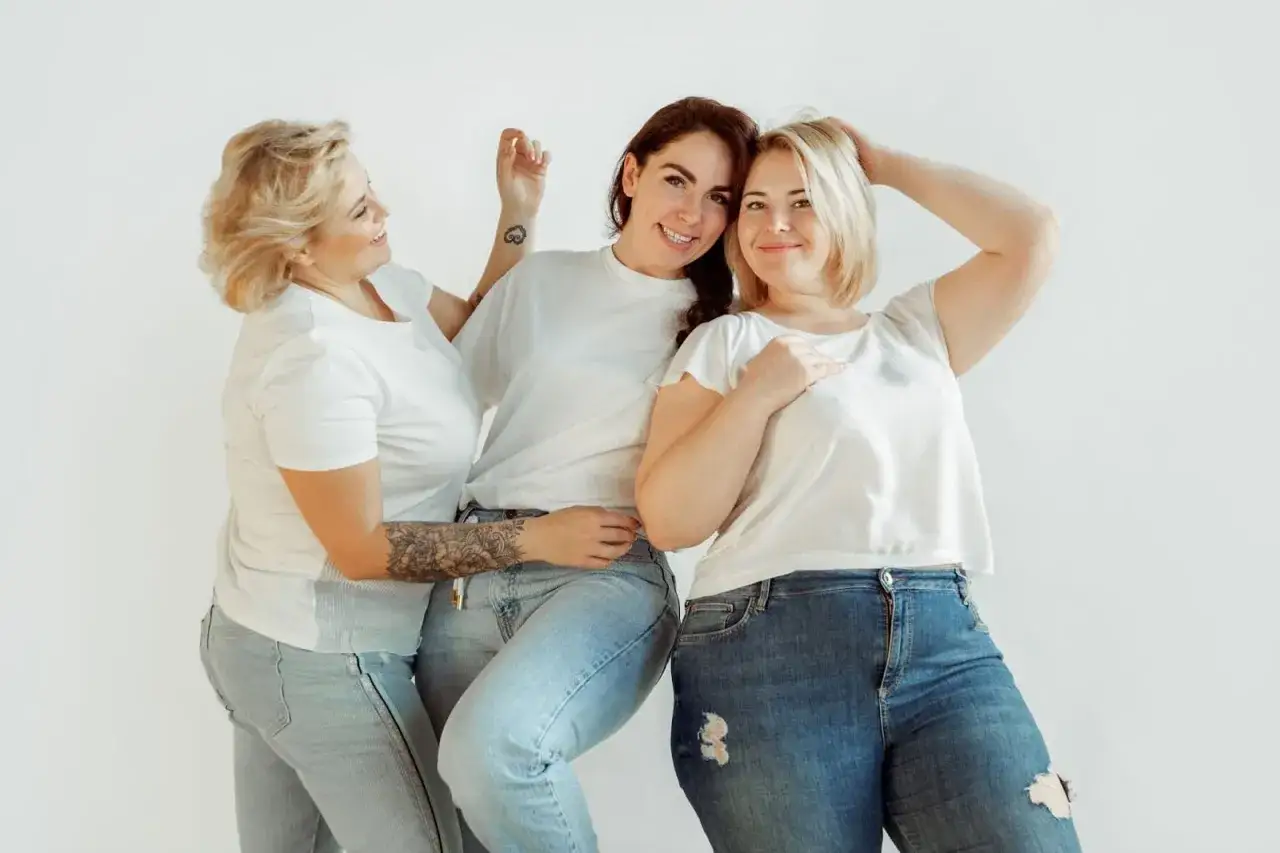 Trois femmes souriantes en jeans et t-shirts blancs. La question 