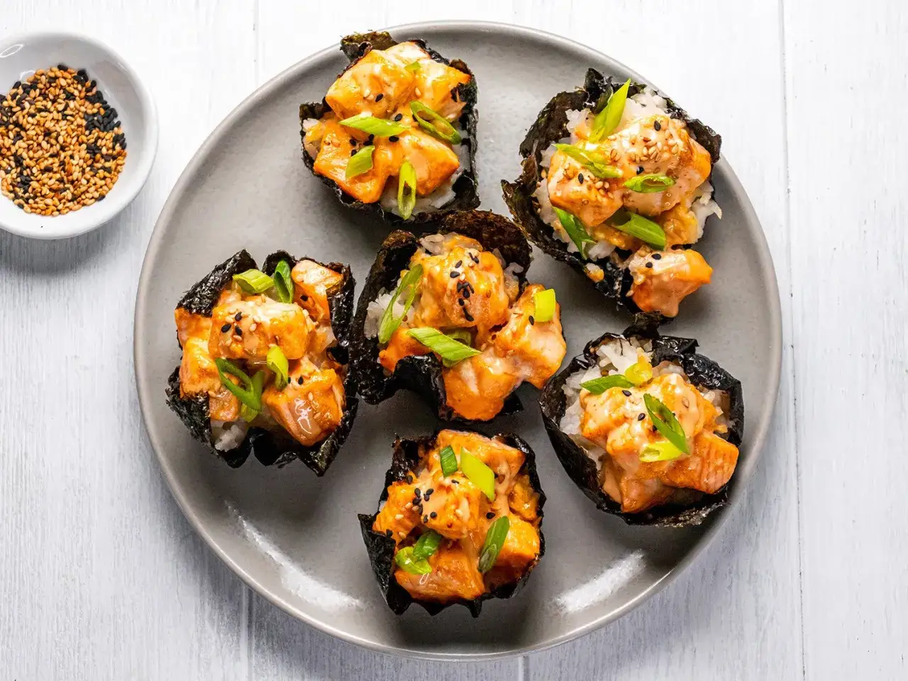Pięć kuszących miseczek z nori, ryżu i sushi z pieczonym łososiem, posypanych szczypiorkiem i sezamem.