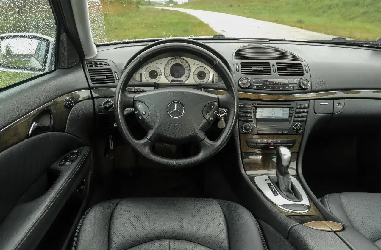 Wnętrze Mercedesa E Klasa 2004 z czarną skórzaną tapicerką, drewnianymi wstawkami i kluczykami w stacyjce.