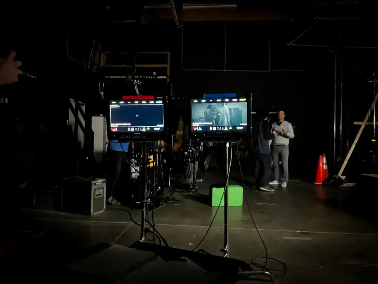Na plan filmowy w ciemnym studiu widać dwa monitory podglądowe, sprzęt i ludzi.