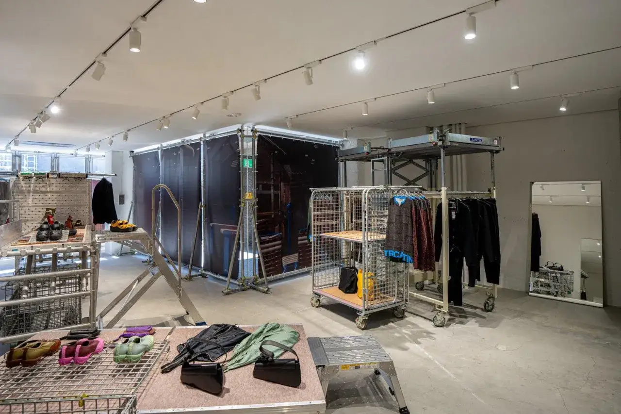 Kiko Kostadinov Kollektion in einem minimalistischen Pop-up-Store. Kleidung und Schuhe sind auf Metallst&auml;ndern und Gittern ausgestellt.