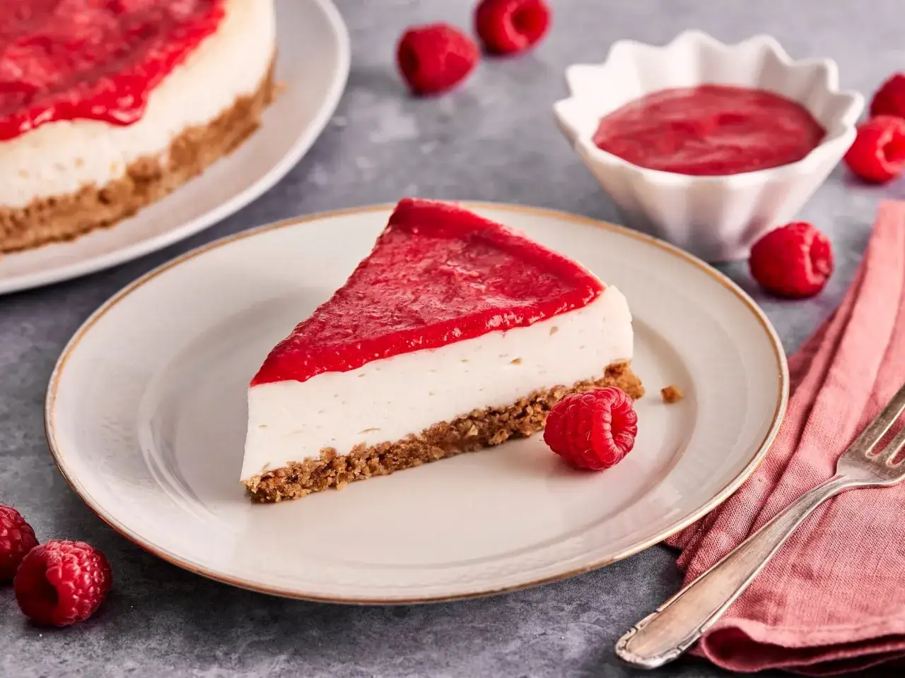 Ein Stück cremiger, veganer Cheesecake mit fruchtigem Himbeerspiegel und frischen Himbeeren.