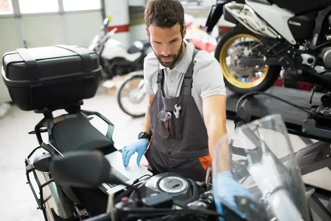 Mechanik w warsztacie wykonuje przegląd motocykla po terminie, korzystając z laptopa.