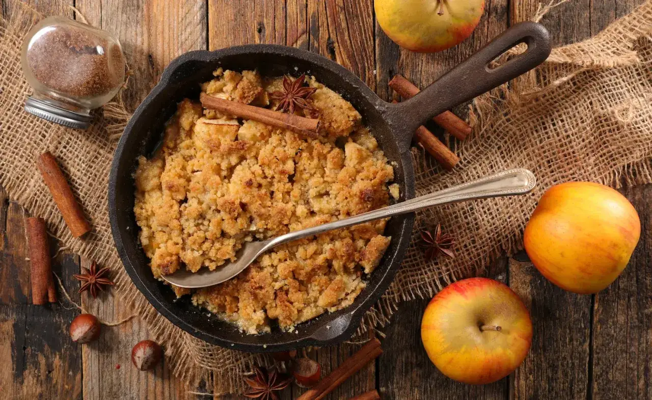 Un d&eacute;licieux crumble aux pommes, dor&eacute; et croustillant, servi dans une po&ecirc;le en fonte, avec des pommes fra&icirc;ches, des b&acirc;tons de cannelle et des anis &eacute;toil&eacute;s.