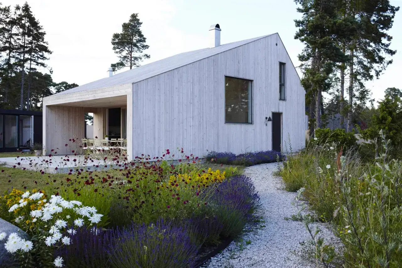 Ett modernt tr&auml;hus med siox trall omgivet av en blomstrande tr&auml;dg&aring;rd och grusg&aring;ng.