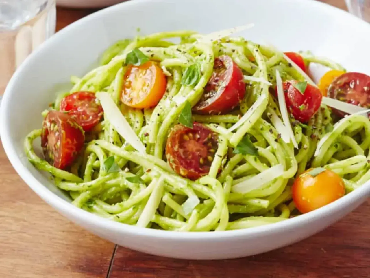 Pyszna pasta z awokado z pomidorkami koktajlowymi i parmezanem, podana w białej misce na drewnianym blacie.