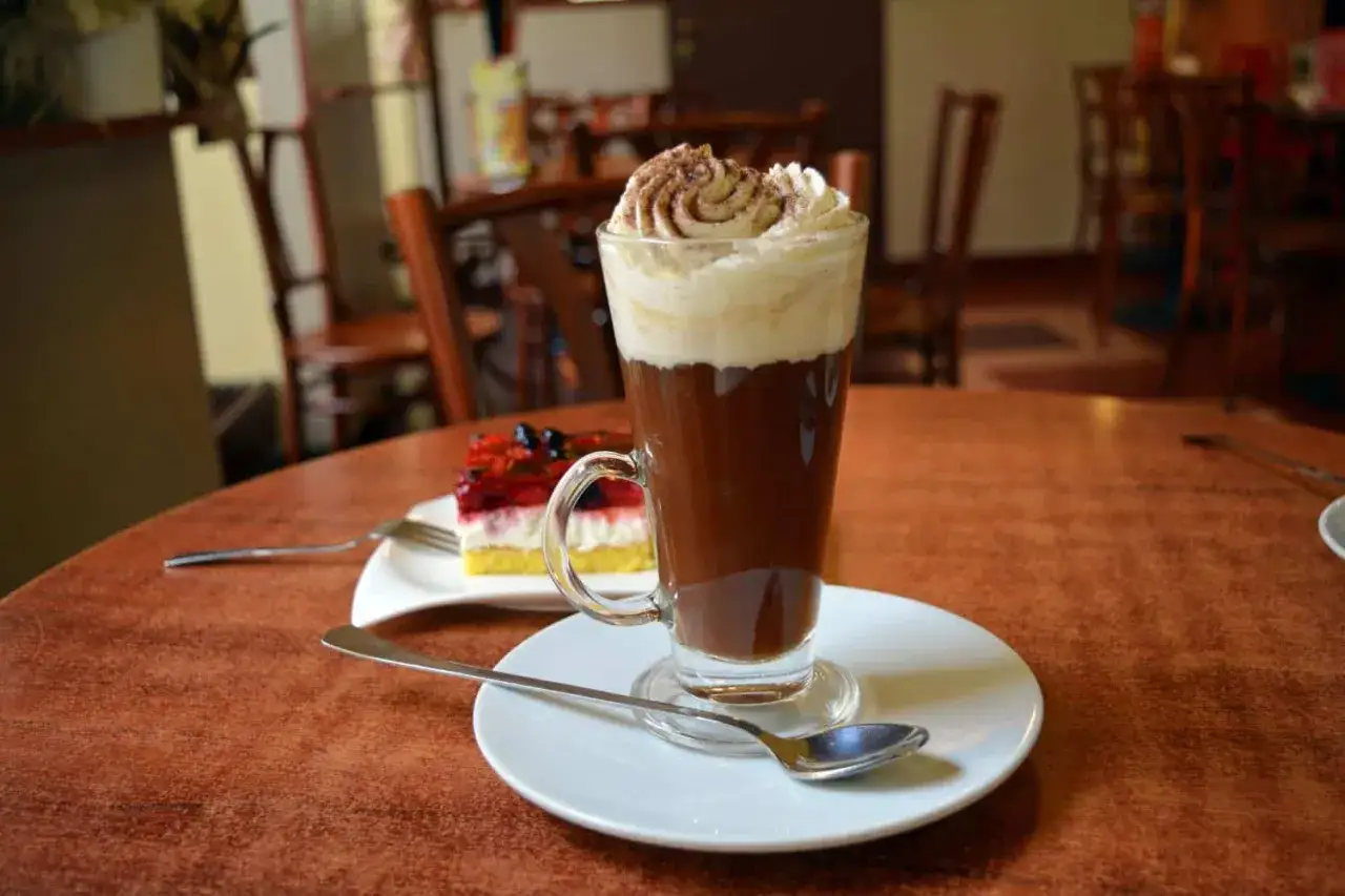 Ein köstlicher kleiner brauner Kaffee mit Sahnehaube und ein Stück Kuchen mit Beeren auf einem Tisch im Café.