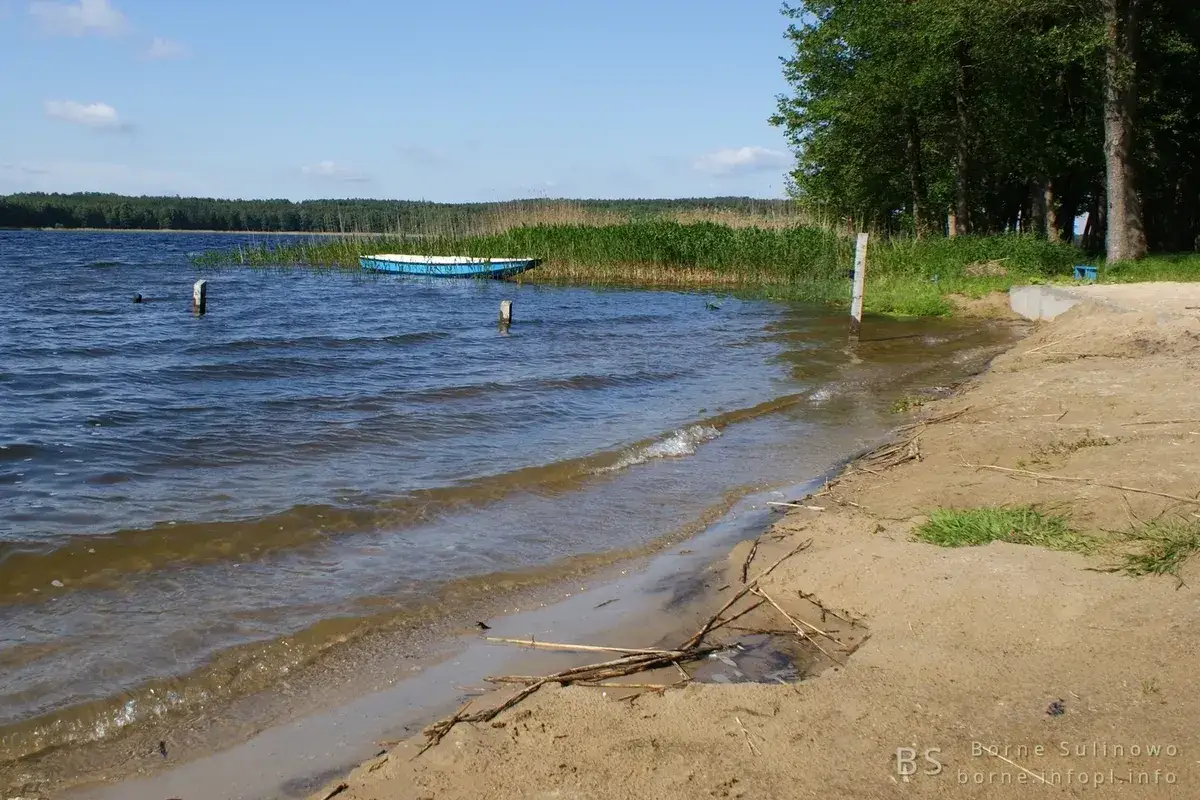 Spokojna plaża nad jeziorem, z łódką przy brzegu i trzcinami. Idealne miejsce na relaks i odkrywanie uroków Bornego Sulinowa.