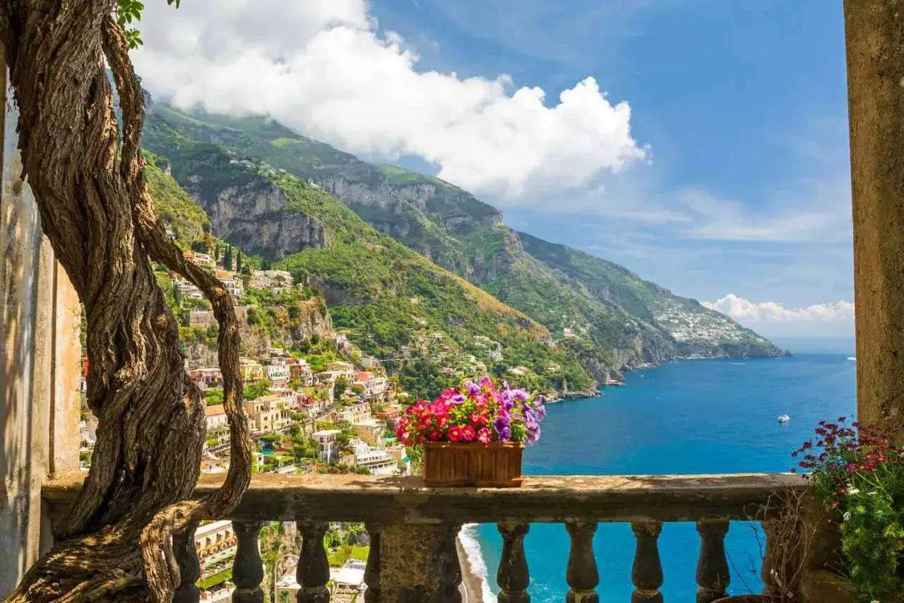 En blomsterprydd balkong med utsikt över den pittoreska italienska kusten. Hus klättrar uppför bergssluttningen mot det glittrande havet.