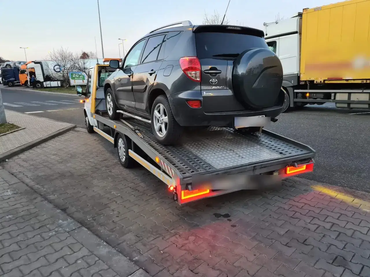 Holowanie na autostradzie: ciemnoszary Toyota RAV4 na lawecie, obok ciężarówki.