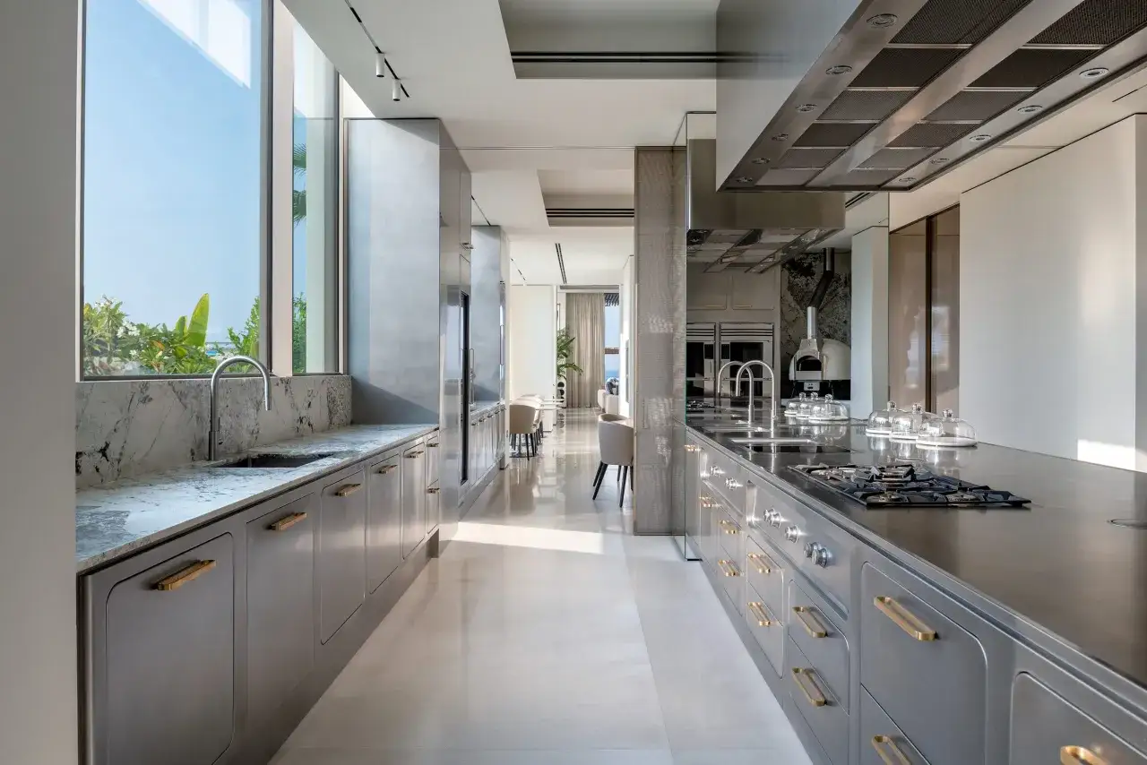 Cucina moderna con isola centrale e bancone in acciaio inox, pensili grigi con maniglie dorate e piano in marmo.