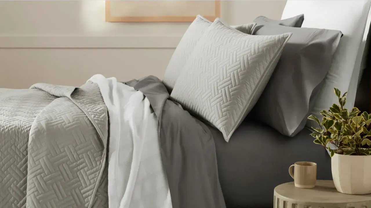 A neatly made bed with grey quilted pillow shams and a textured blanket. You can definitely sleep on pillow shams for a cozy night.