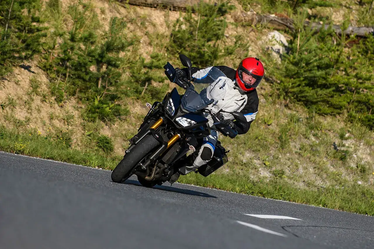 Motocyklista w czerwonym kasku pochyla się na zakręcie, pokonując krętą drogę. Niesamowite wrażenia z jazdy korsyka motocyklem.