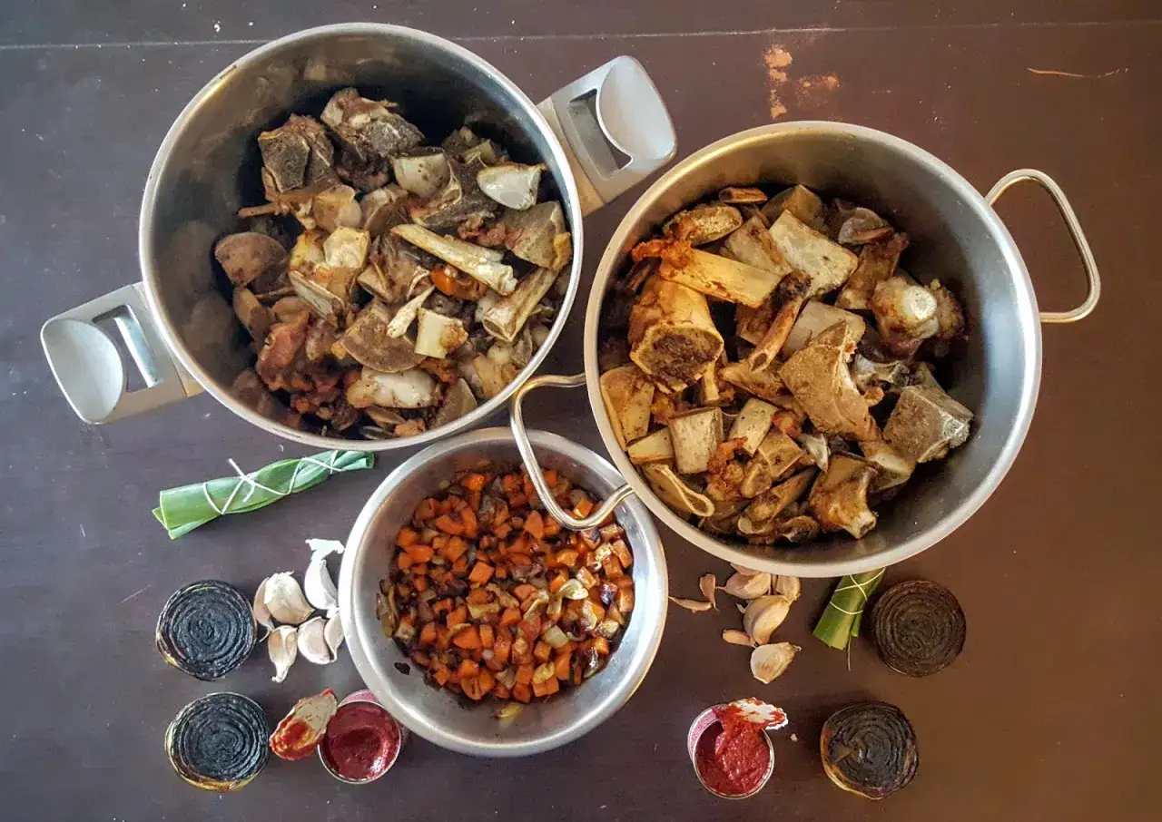 Ossements de veau r&ocirc;tis dans trois casseroles, pr&ecirc;ts pour un riche jus de veau. Carottes coup&eacute;es en d&eacute;s, ail, oignons br&ucirc;l&eacute;s et concentr&eacute; de tomate compl&egrave;tent la sc&egrave;ne.